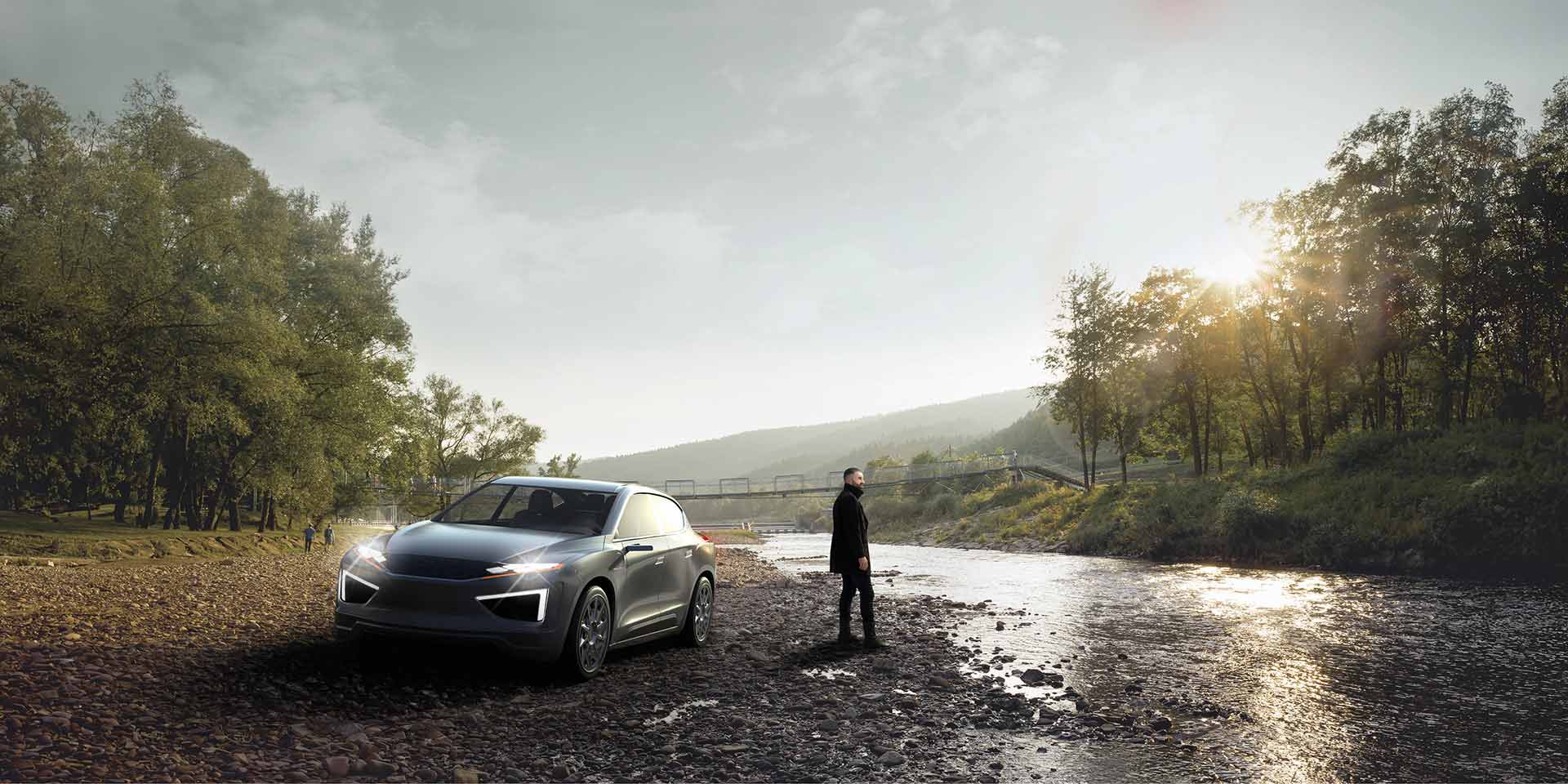 Person standing outside of a vehicle at the edge of a river with tree lined banks