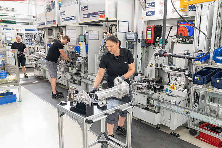 Factory workers assembling automotive parts, with a woman inspecting components in the foreground.